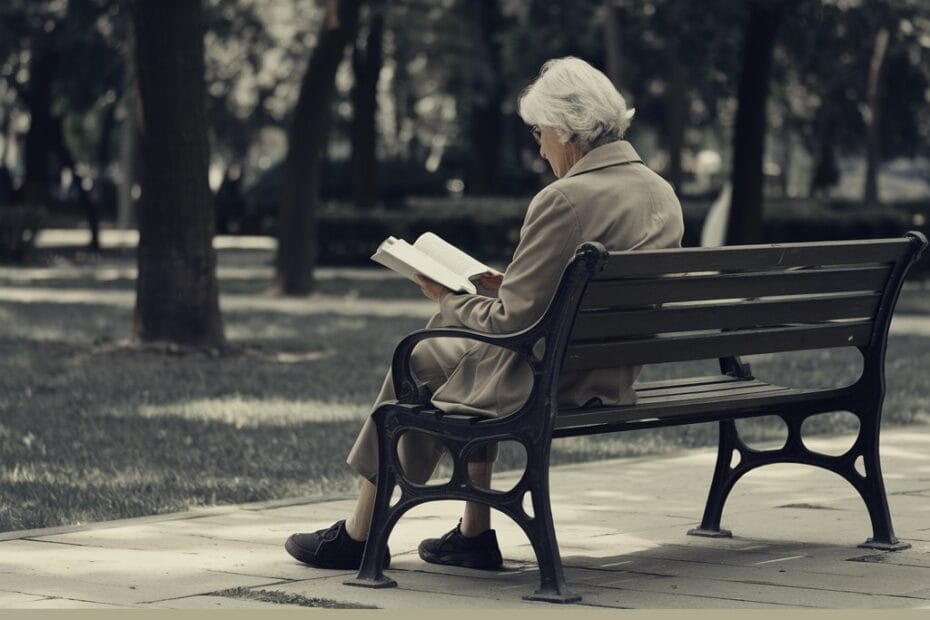 Imagem de um senhor aposentado sentado em um banco de praça, lendo um livro